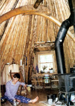Ashirah sits beside the woodstove, which she and Chris use for heating and cooking. The arch visible above her head is one of two that provides structural support for the lodge.